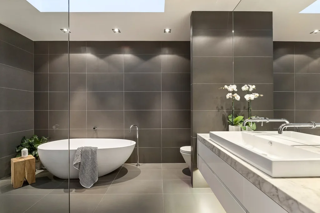 Luxury bathroom with freestanding bathtub, twin basins, and grey tile walls
